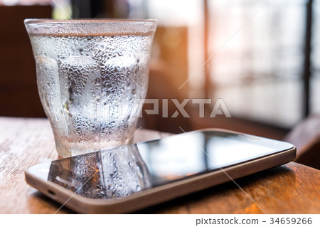 Cold water glass with a smart phone on the table. 34659266