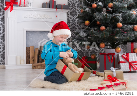 Cute boy in santa hat unwrapping christmas Cute boy in santa hat unwrapping christmas 34668291