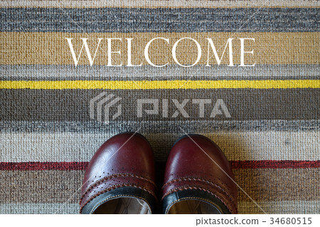 Welcome carpet with leather shoes on it. 34680515