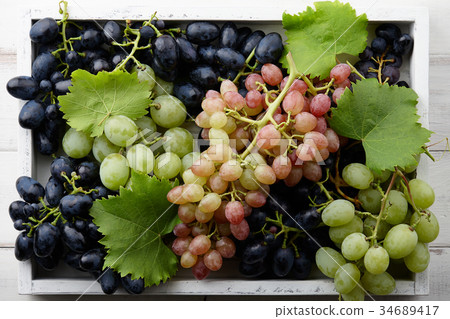 Various grapes with leaves in white wooden tray 34689417