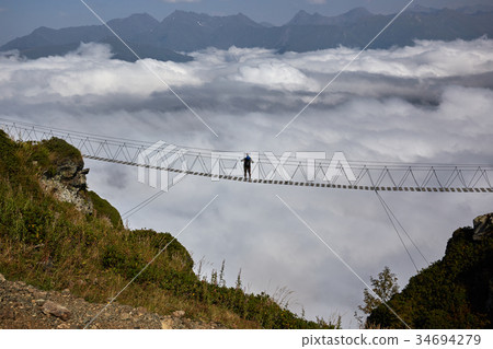 Man walking on suspension bridge and looking at Man walking on suspension bridge and looking at 34694279