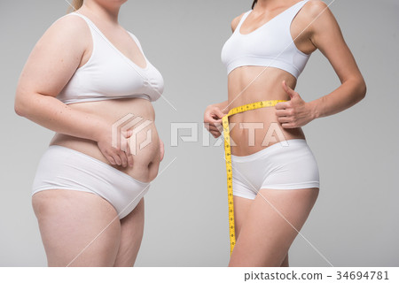 Thin girl measuring her abdomen near fat one 34694781