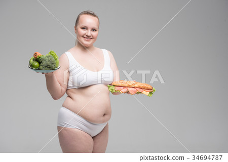 Joyful thick girl choosing between healthy and 34694787
