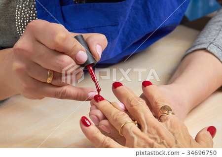 Woman applying red varnish to finger nails. 34696750