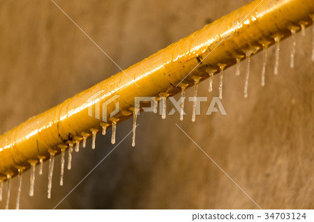 Icicles on a yellow pipe at sunset 34703124