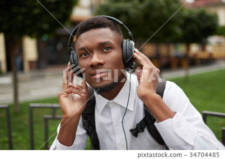 African man resting outdoors and listening music. African man resting outdoors and listening music. 34704485