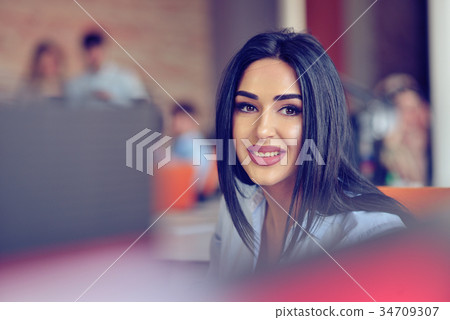 Businesswoman sits at a desk in front of a Businesswoman sits at a desk in front of a 34709307