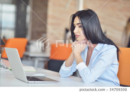 Businesswoman sits at a desk in front of a Businesswoman sits at a desk in front of a 34709308