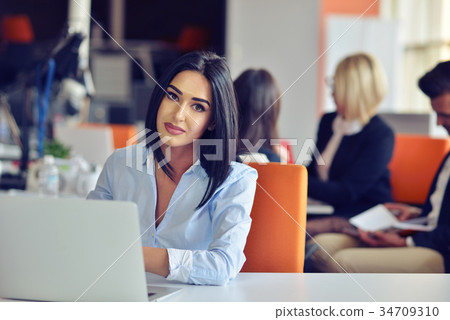 Businesswoman sits at a desk in front of a Businesswoman sits at a desk in front of a 34709310