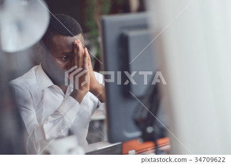 Tired African man sitting at a office after a hard Tired African man sitting at a office after a hard 34709622