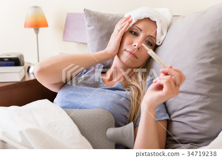Sick woman with fever checking her temperature 34719238