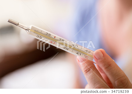 Hand holding analog medical thermometer 34719239