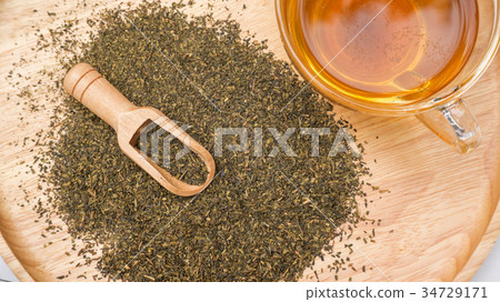 A cup of tea and a green tea leaf on a table. A cup of tea and a green tea leaf on a table. 34729171
