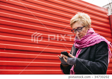 Woman texting at red wall Woman texting at red wall 34730202