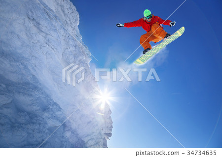 Snowboarder jumping against blue sky 34734635