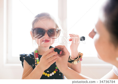 Mother painting lips of her cute little daughter 34736784