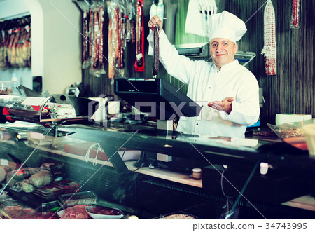 Male seller posing with wursts in butchery 34743995