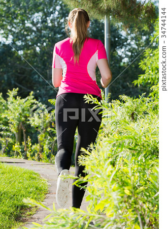 Smiling adult female in pink T-shirt is jogging back Smiling adult female in pink T-shirt is jogging back 34744144