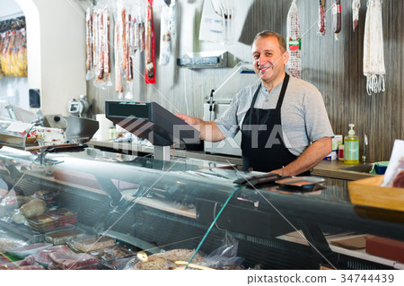 butcher with smoked meat at counter 34744439