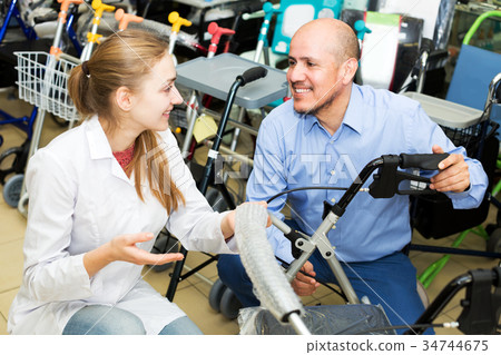 Female consultant offering wheelchair to mature customer Female consultant offering wheelchair to mature customer 34744675