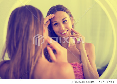 woman examining her face by looking at it in mirror 34744754