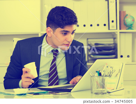 Young man is working at a computer and drinking coffee 34745005