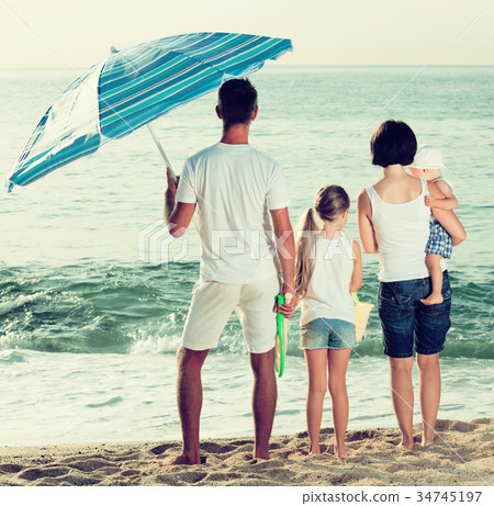 back view on family of four standing on beach . 34745197