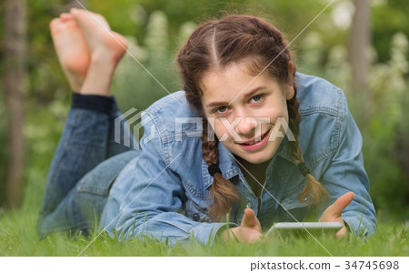 smiling young female using digital tablet while lying in outdoors 34745698