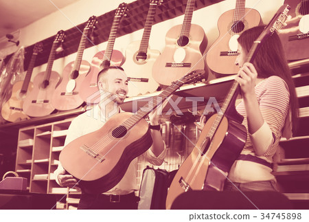Young couple choosing acoustic guitar in shop Young couple choosing acoustic guitar in shop 34745898