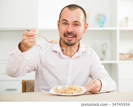 Positive young man eating porridge Positive young man eating porridge 34745934