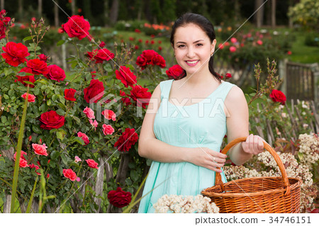portrait of young female holding a basket near roses in outdoors 34746151
