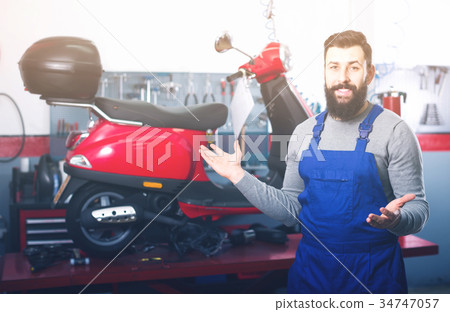 smiling man worker displaying his workplace in motorcycle workshop smiling man worker displaying his workplace in motorcycle workshop 34747057