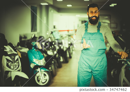 Smiling male worker demonstrating motorcycles Smiling male worker demonstrating motorcycles 34747462