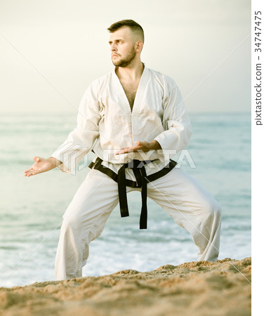 Guy doing karate poses at sunset sea shore 34747475
