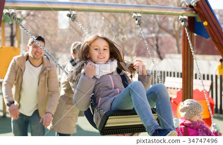 Parents watching little daughters swinging 34747496