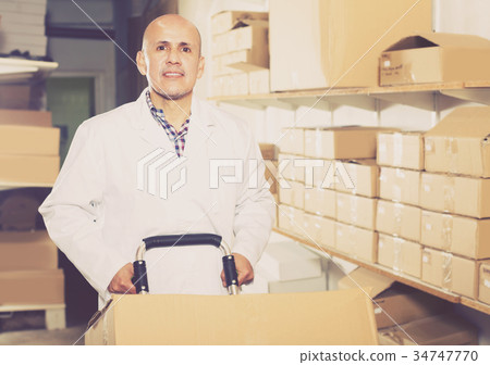 Mature male worker standing with cart at workplace Mature male worker standing with cart at workplace 34747770