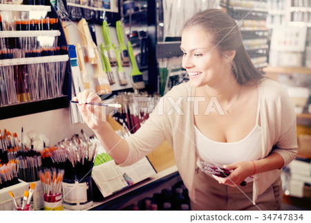 young woman selecting brushes in shop. 34747834