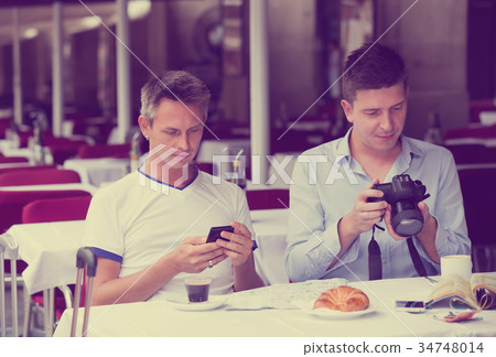 tourists drinking coffee and looking photos 34748014