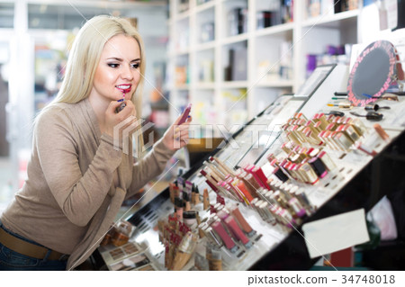 Portrait of young blondie selecting lipstick in store 34748018