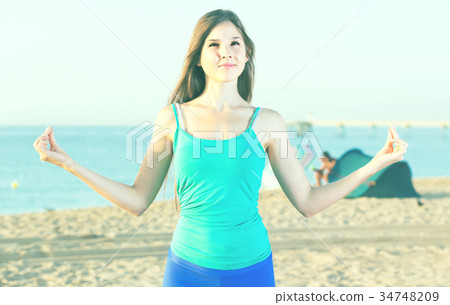 Young woman in blue T-shirt is standing and practicing asana Young woman in blue T-shirt is standing and practicing asana 34748209