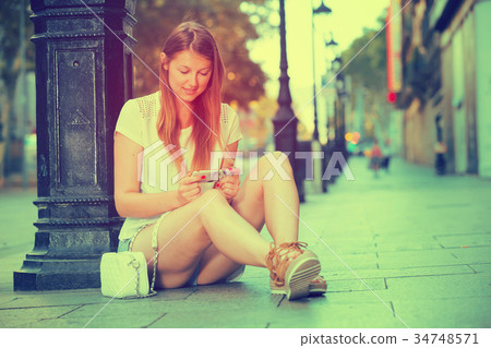 Woman sitting with phone near lamp post 34748571