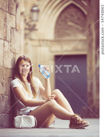 Woman sitting near old stone wall drinking water Woman sitting near old stone wall drinking water 34748665