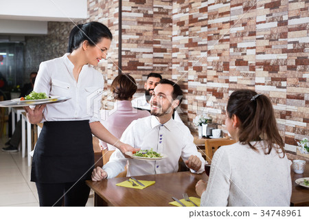 Female waiter bringing order to visitors in country restaurant Female waiter bringing order to visitors in country restaurant 34748961