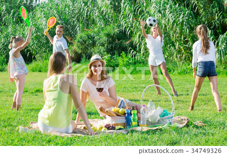 females on picnic outdoors on background with children playing active games 34749326