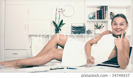 Cheerful manager female relaxing on desk in office Cheerful manager female relaxing on desk in office 34749837