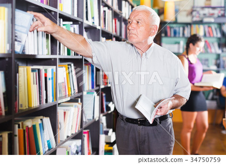 Portrait of mature man is choosing book for reading 34750759