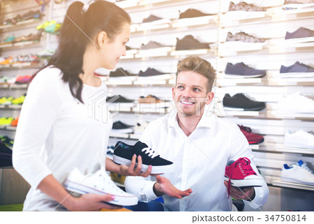 Smiling seller demonstrating sneakers to female 34750814