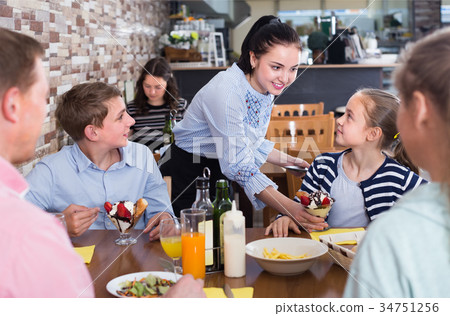 Young brunette waitress serving satisfied family in family cafe Young brunette waitress serving satisfied family in family cafe 34751256