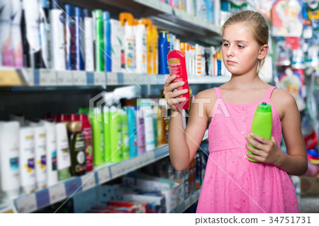 Girl teenager choosing shampoo and conditioner at shop 34751731