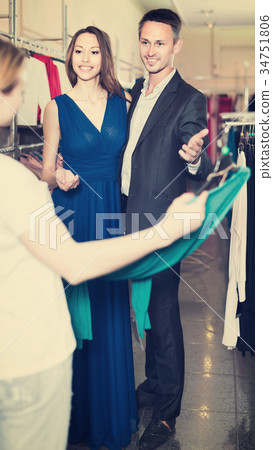 woman shop assistant offering dress variants to cheerful pair 34751806
